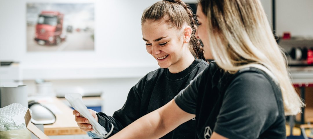 Two cheerful trainees in black work clothes pack a box together.