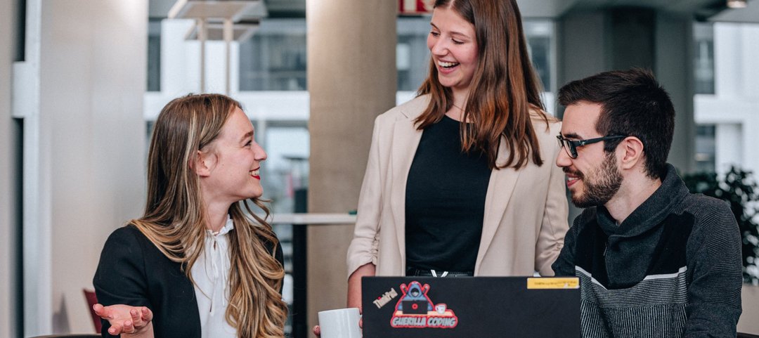 Laughing young graduates in a team discussion as they work together on the laptop in front of them.