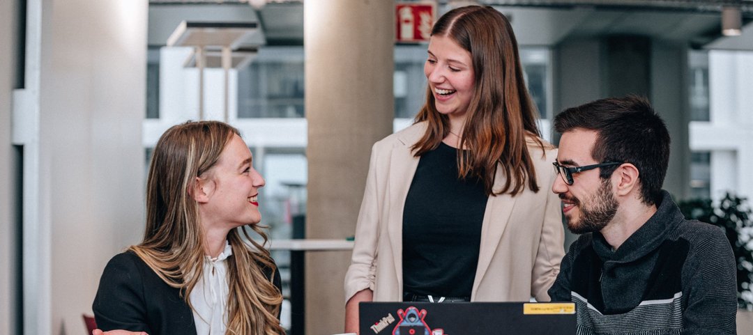 Laughing young graduates in a team discussion as they work together on the laptop in front of them.
