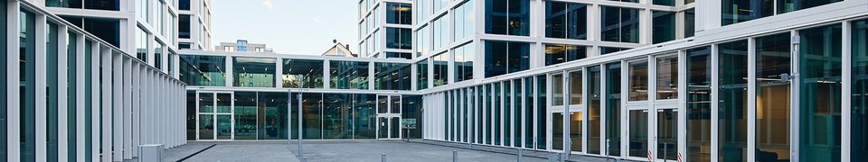 View of the Daimler Truck headquarters in Leinfelden with large glass facades and the company logo in the courtyard in the foreground.