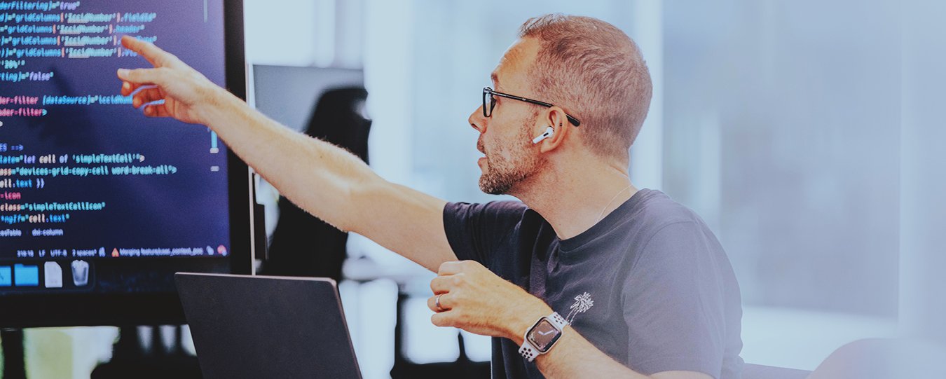 A software developer points to a code on a screen during a meeting.