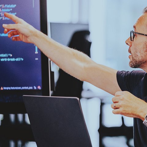 A software developer points to a code on a screen during a meeting.