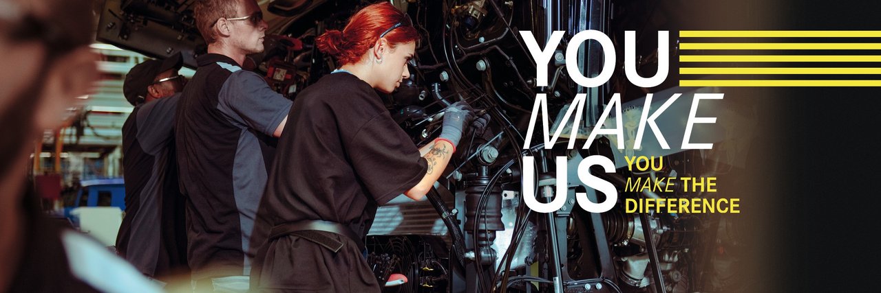 Young employees assemble parts on a truck in Daimler Truck Production - teamwork and commitment in a holiday job. Text in the picture: ‘You make us - You make the difference.’