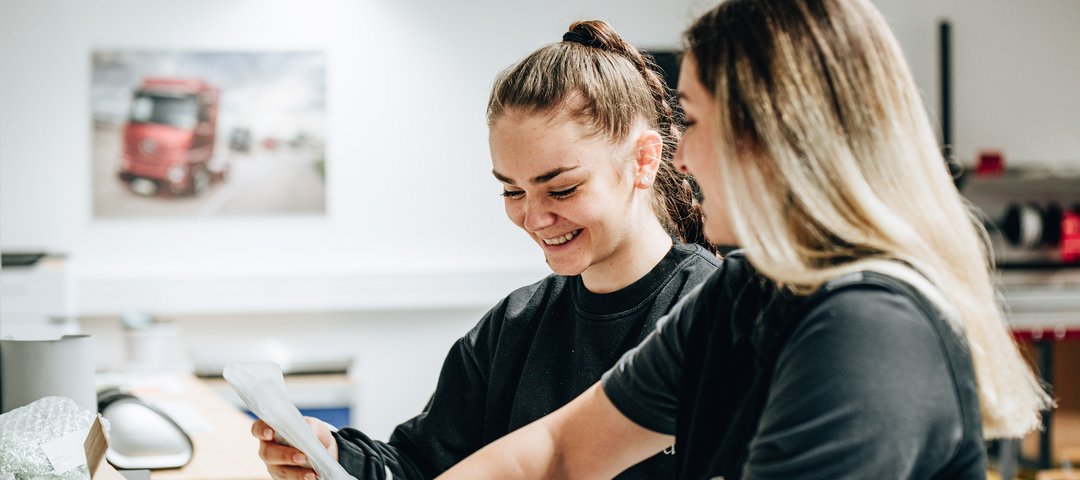 Two cheerful trainees in black work clothes pack a box together.