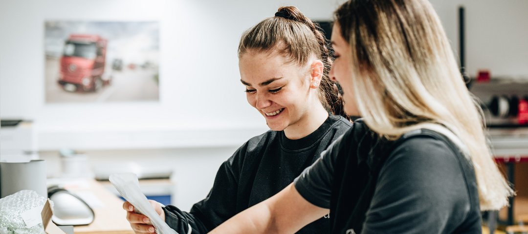 Two cheerful trainees in black work clothes pack a box together.