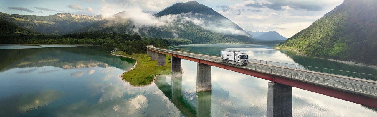 Mercedes-Benz eActros drives over a bridge over a lake in the mountains
