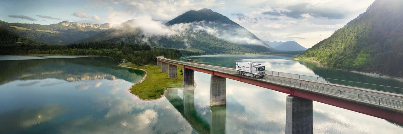 Mercedes-Benz eActros drives over a bridge over a lake in the mountains